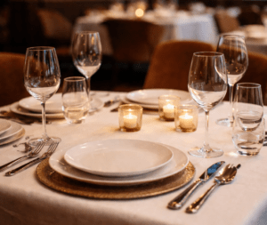 Image qui illustre l'article "créer un site restaurant" Table dressée dans un restaurant gastronomique avec verres à vin, assiettes blanches et bougies